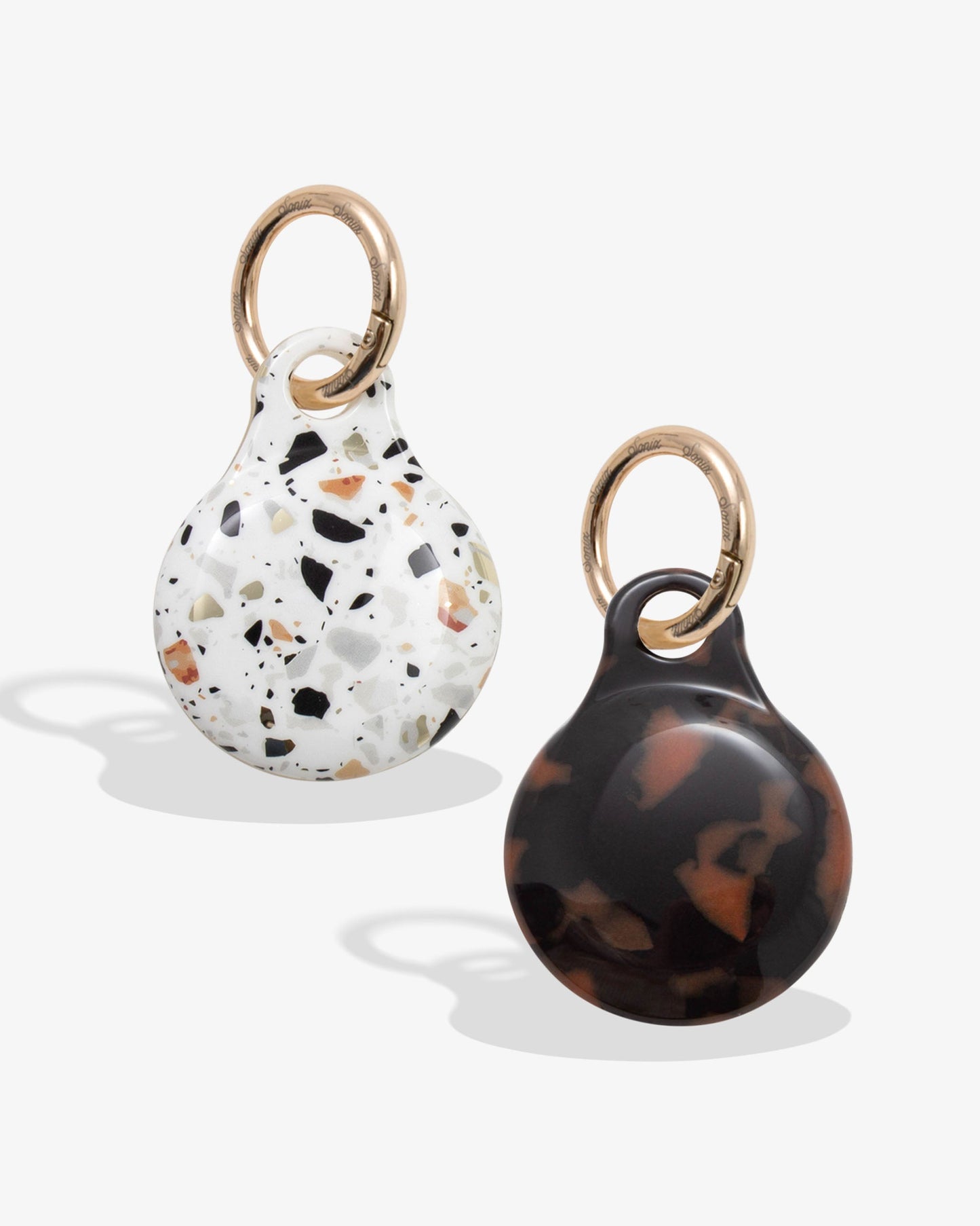 plastic airtag covers with gold rings - one is confetti with browns, black, blues, and oranges and one is brown tortoise
