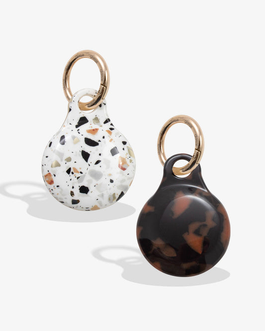 plastic airtag covers with gold rings - one is confetti with browns, black, blues, and oranges and one is brown tortoise