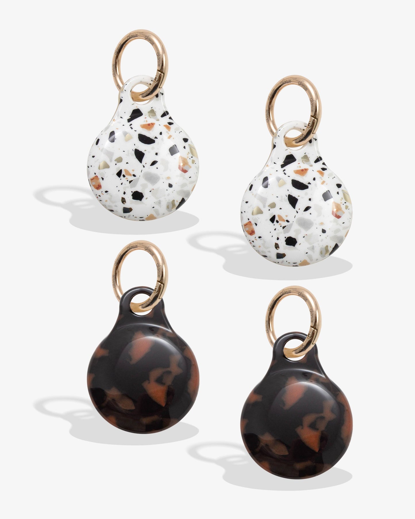 plastic airtag covers with gold rings - one is confetti with browns, black, blues, and oranges and one is brown tortoise