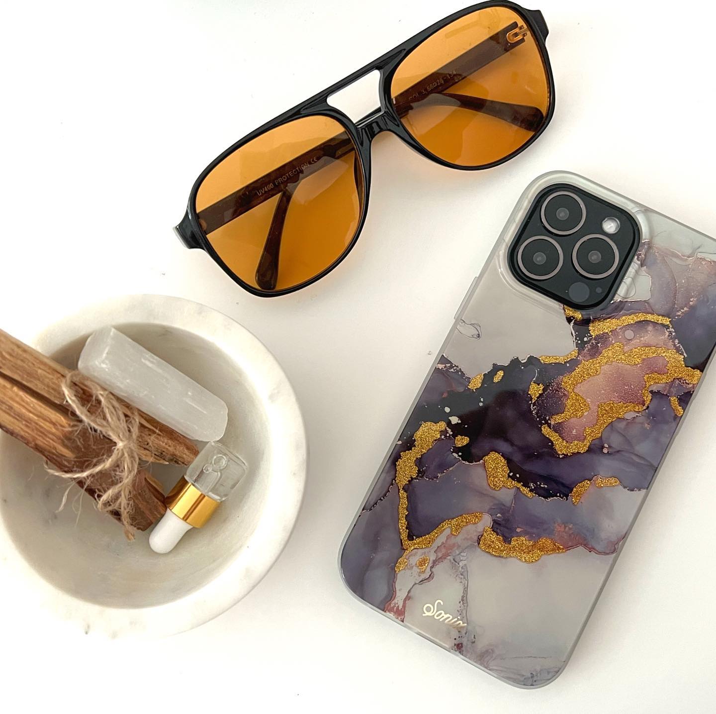 an intergalactic purple and dark colored design with gold glitter to bring out-of-this-world elements shown on an iphone 12 lying on a blank white table with sunglasses and a bowl