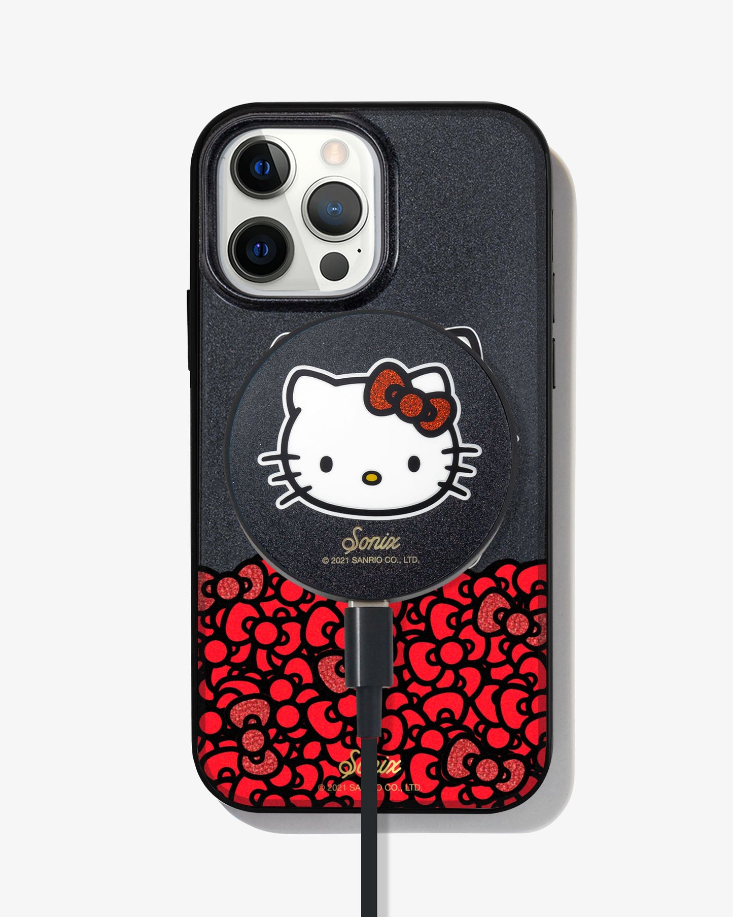 black glitter and Hello Kitty sitting on a bundle of her iconic red bows shown on a iphone 12 pro with a hello kitty magnetic link charger attached to the back
