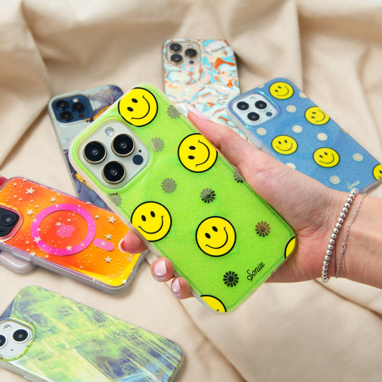 The clear yellow case infused with iridescent glitter features happy faces and signature gold foil flowers shown on an iphone being held by a hand