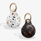 plastic airtag covers with gold rings - one is confetti with browns, black, blues, and oranges and one is brown tortoise