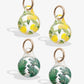 clear airtag cover with yellow lemons and green leaves with gold ring; clear airtag case with green palm leaves with gold foil detail