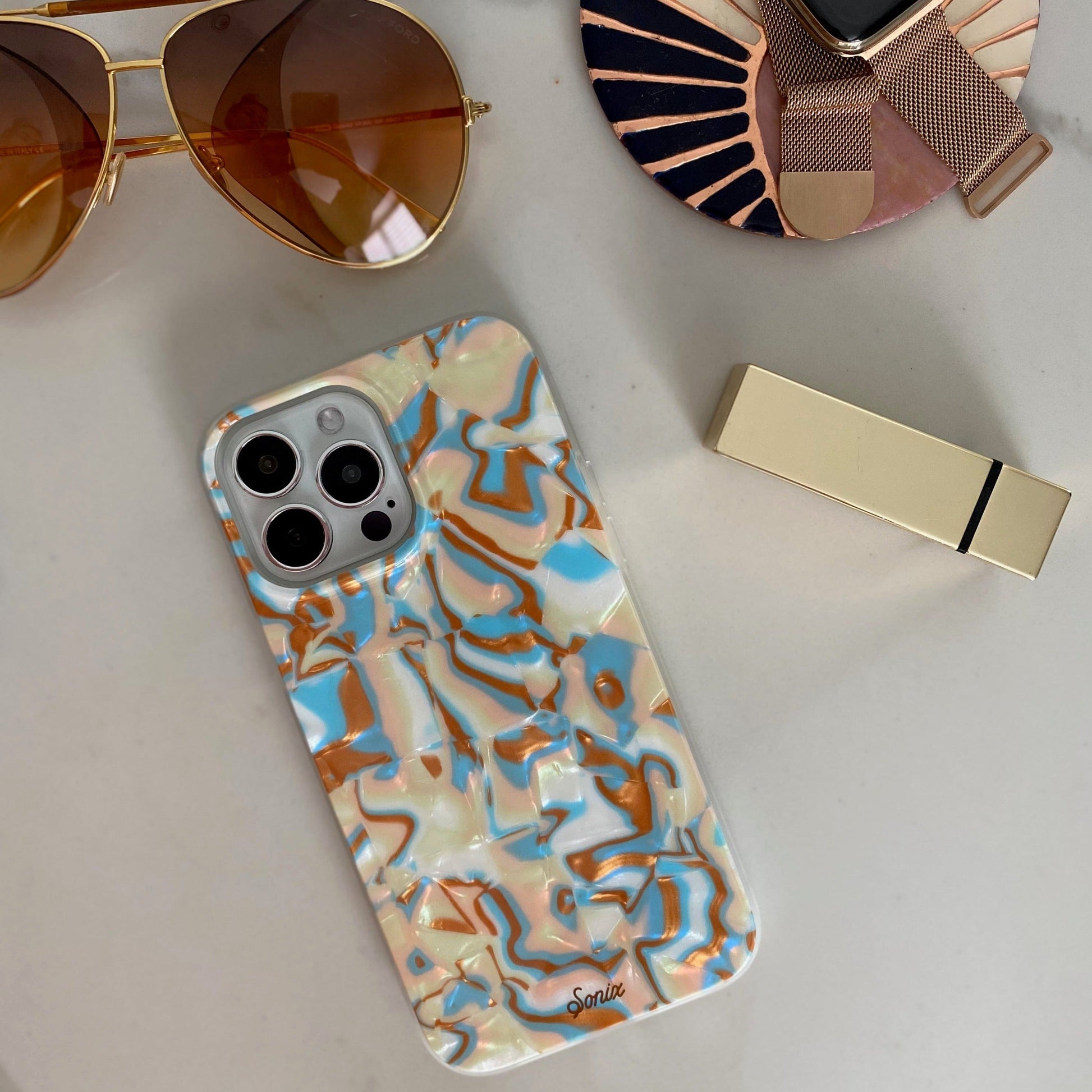 metallic oranges, blues, and cream colors in a wavy 70's pattern shown on an iphone from a flat lay angle 