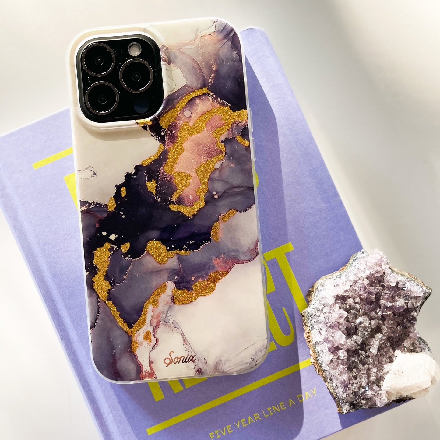 an intergalactic purple and dark colored design with gold glitter to bring out-of-this-world elements shown on an iphone 12 lying on a purple book with an amethyst crystal next to it