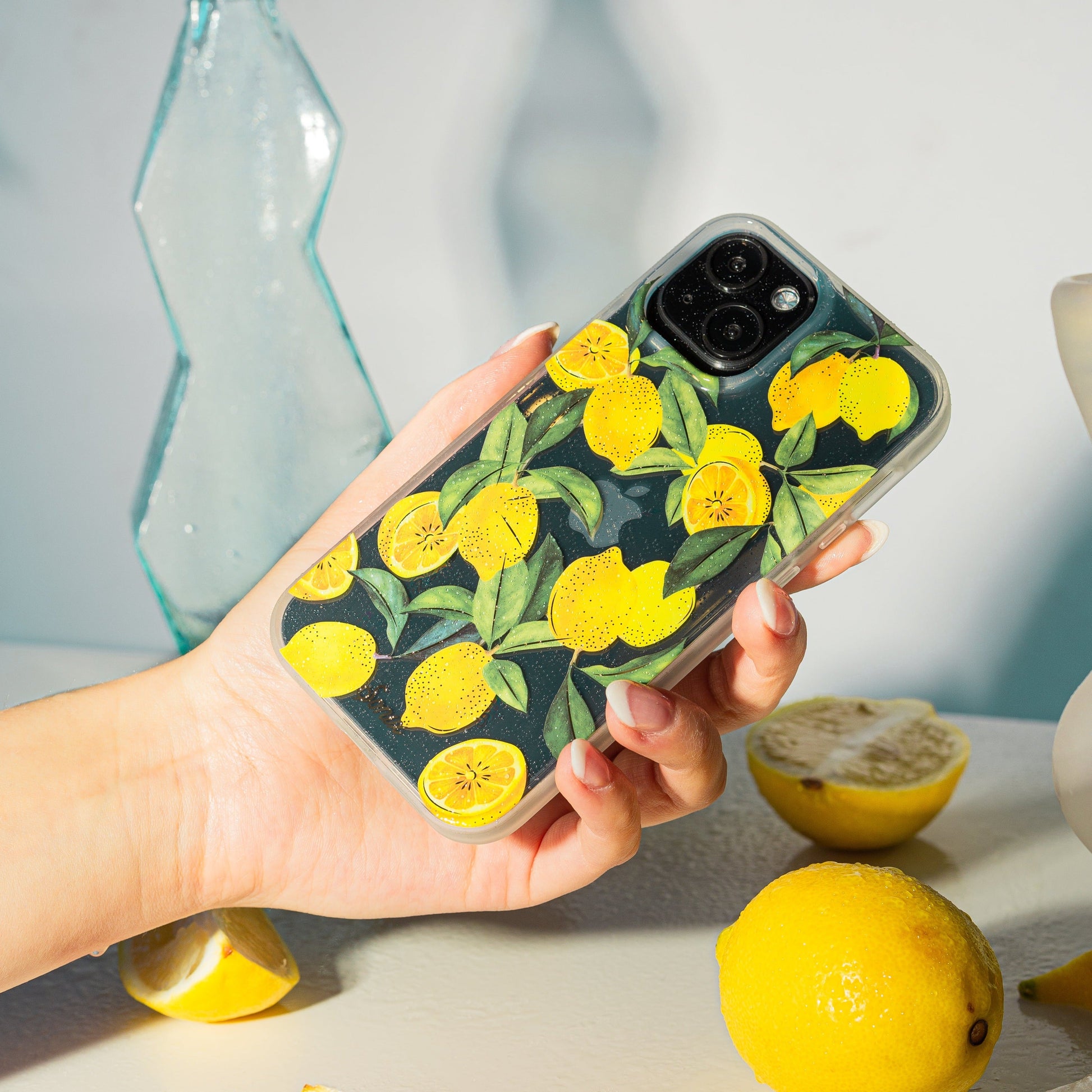 Lemons with green foliage and gold foiling shown on a black iphone 13 with a hand holding the phone