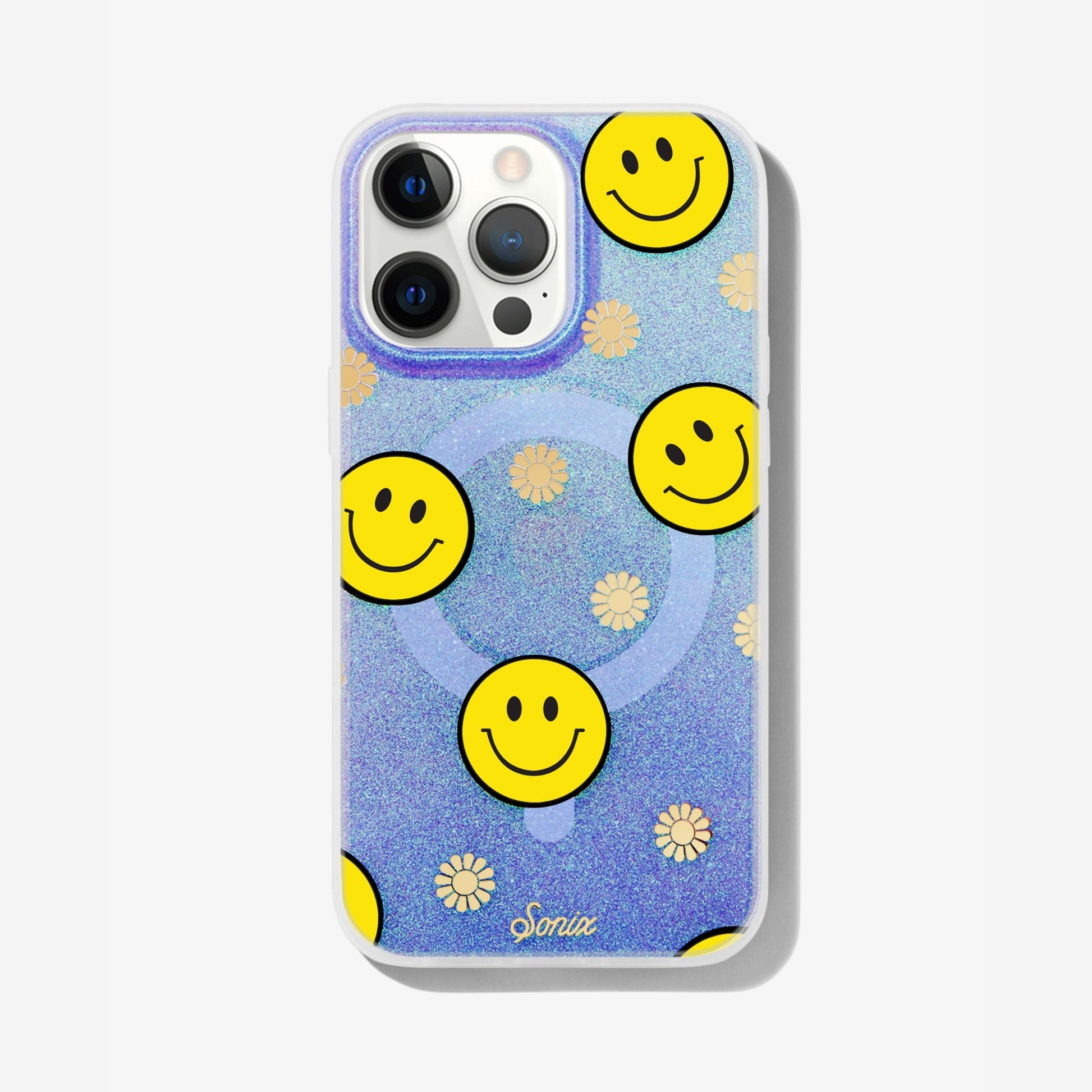 The clear purple case infused with iridescent glitter features happy faces and signature gold foil flowers shown on an iphone 12