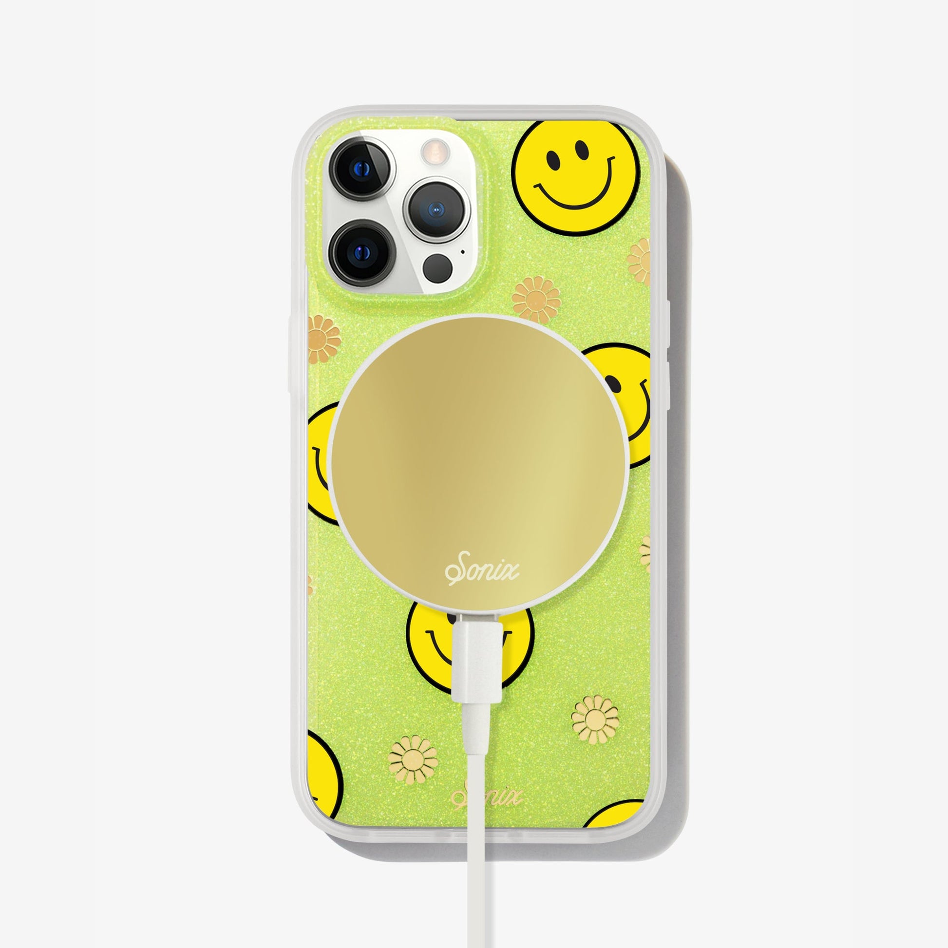 The clear yellow case infused with iridescent glitter features happy faces and signature gold foil flowers shown on an iphone with a gold maglink charger on the back