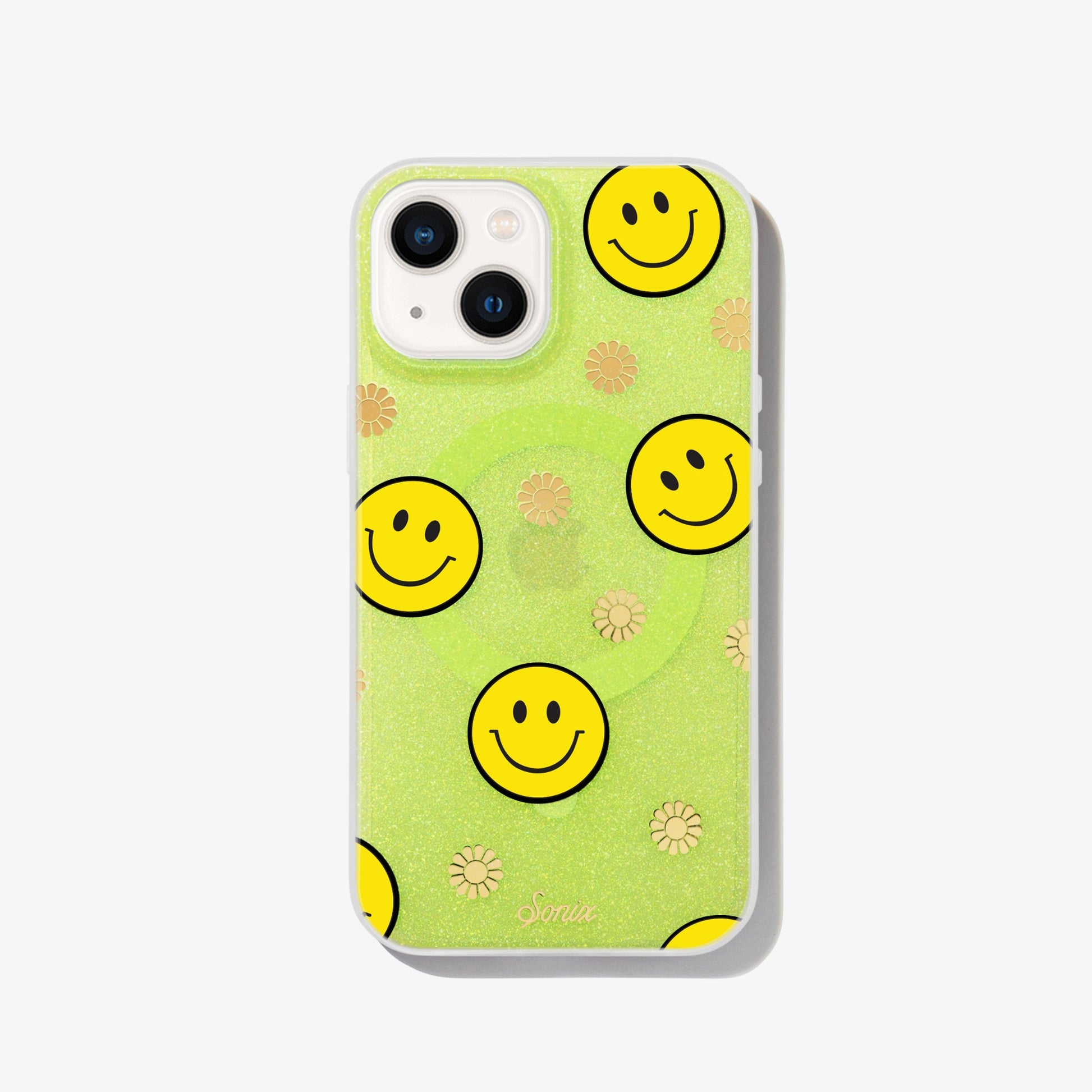 The clear yellow case infused with iridescent glitter features happy faces and signature gold foil flowers shown on an iphone 12