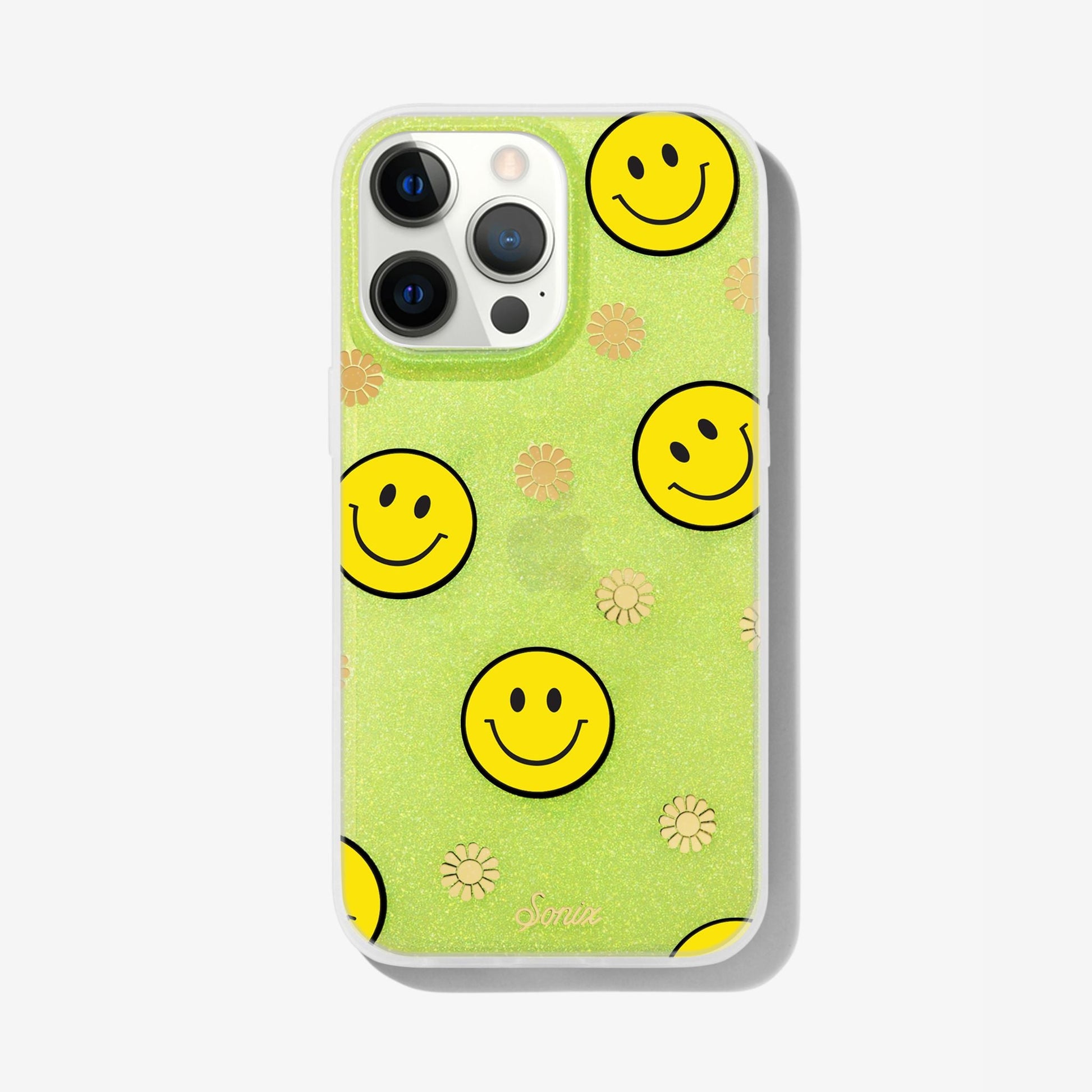 The clear yellow case infused with iridescent glitter features happy faces and signature gold foil flowers shown on an iphone 13 pro max