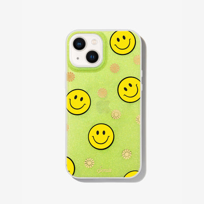 The clear yellow case infused with iridescent glitter features happy faces and signature gold foil flowers shown on an iphone 13