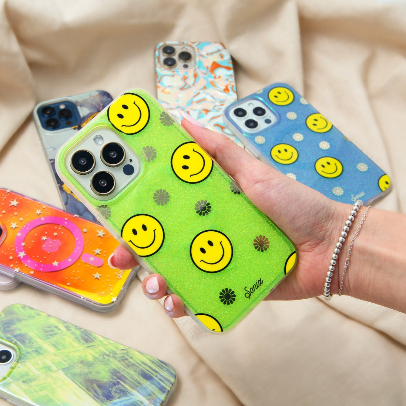 The clear yellow case infused with iridescent glitter features happy faces and signature gold foil flowers shown on an iphone being held by a hand